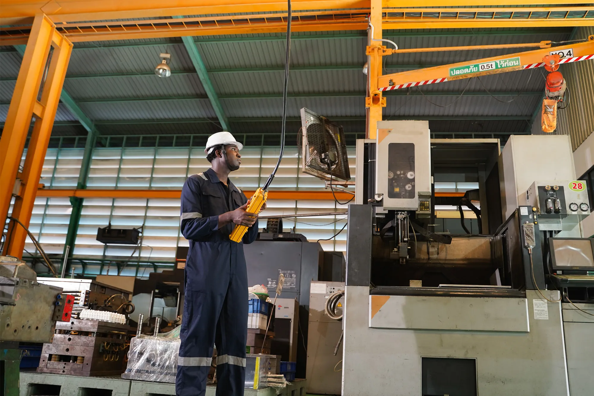 Industrial worker in protective gear guiding a massive white bulk material bag suspended by a yellow hoist.